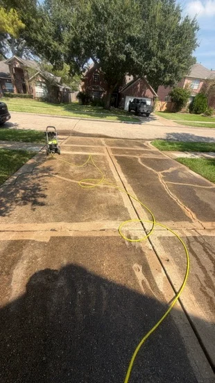 Driveway cleaning underway, with hose and equipment on the concrete